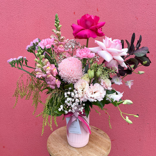 A beautiful flower arrangement featuring shades of pink including a prominent rose in a cylindrical vase.